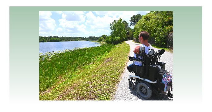 Man in Power Wheelchair looking out at a lake from a paved pathway